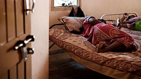 Eine schwangere Frau liegt auf dem Bett. Sie ist eine Leihmutter in Indien. 