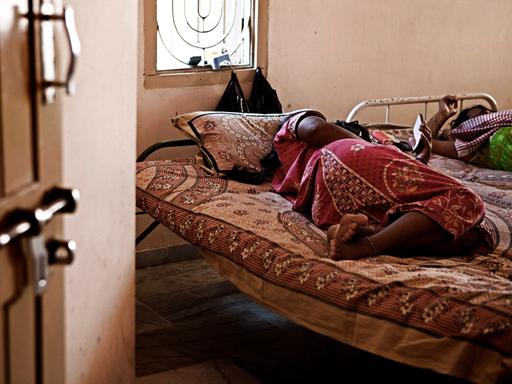 Eine schwangere Frau liegt auf dem Bett. Sie ist eine Leihmutter in Indien. 