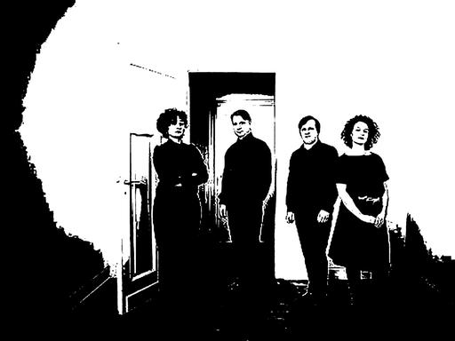 Die Mitglieder des Quartetts stehen in einem Raum ohne ihre Instrumente und schauen ernst in die Kamera.