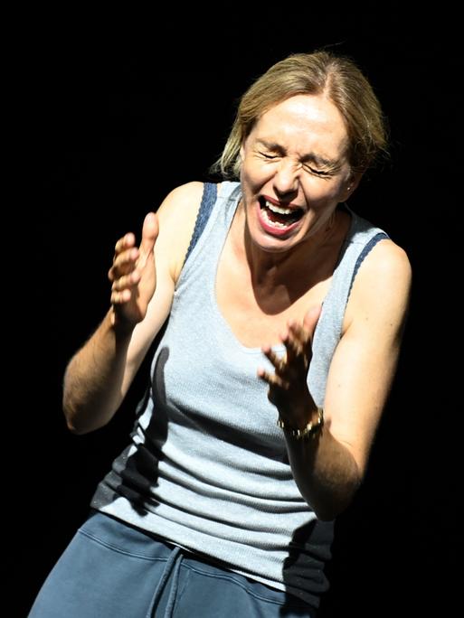 Milo Rau steht schreiend auf einer Theaterbühne vor schwarzem Hintergrund