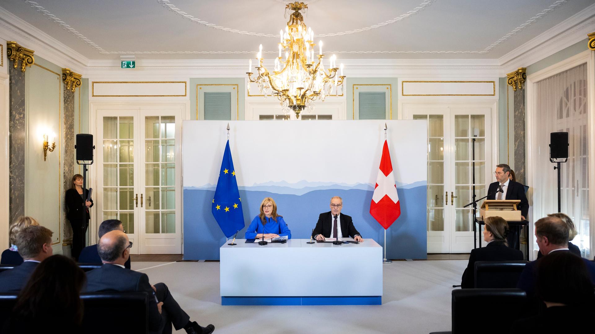 Ekaterina Zachariewa und Guy Parmelin sitzen an einem Tisch, hinter ihnen sind die Fahnen der EU und der Schweiz.