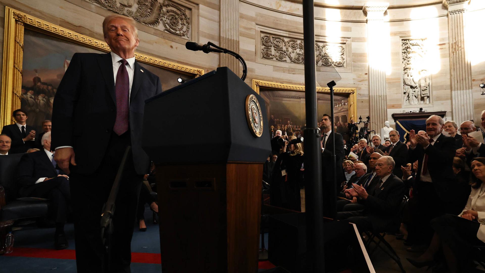 Donald Trump steht an einem Rednerpult im Kapitol und lächelt in die Kamera.