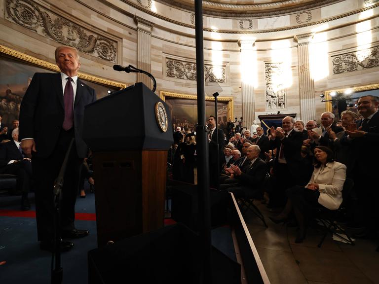 Donald Trump steht an einem Rednerpult im Kapitol und lächelt in die Kamera.