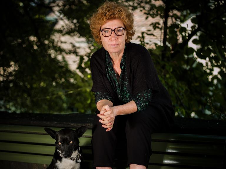 Zora del Buono hockt auf der Lehne einer Parkbank, zu ihren Füßen sitzt ihr Hund.
