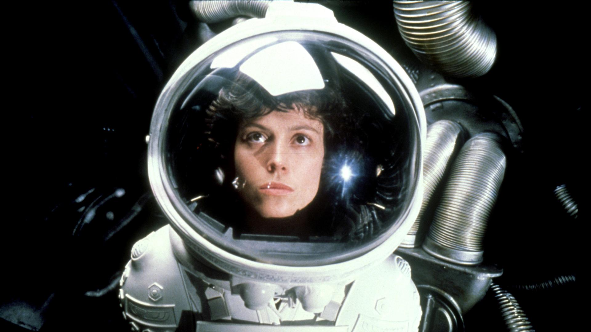 Sigourney Weaver als Officer Ellen Ripley trägt einen Raumanzug und schaut durch das Sichtfenster ihres Helms nach oben.