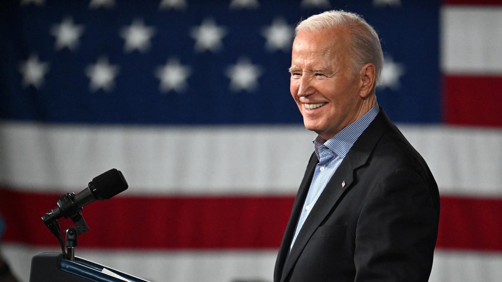 Joe Biden steht an einem Rednerpult und lächelt. Im Hintergrund die US-Flagge. Joe Biden steht an einem Rednerpult und lächelt. Im Hintergrund die US-Flagge.
