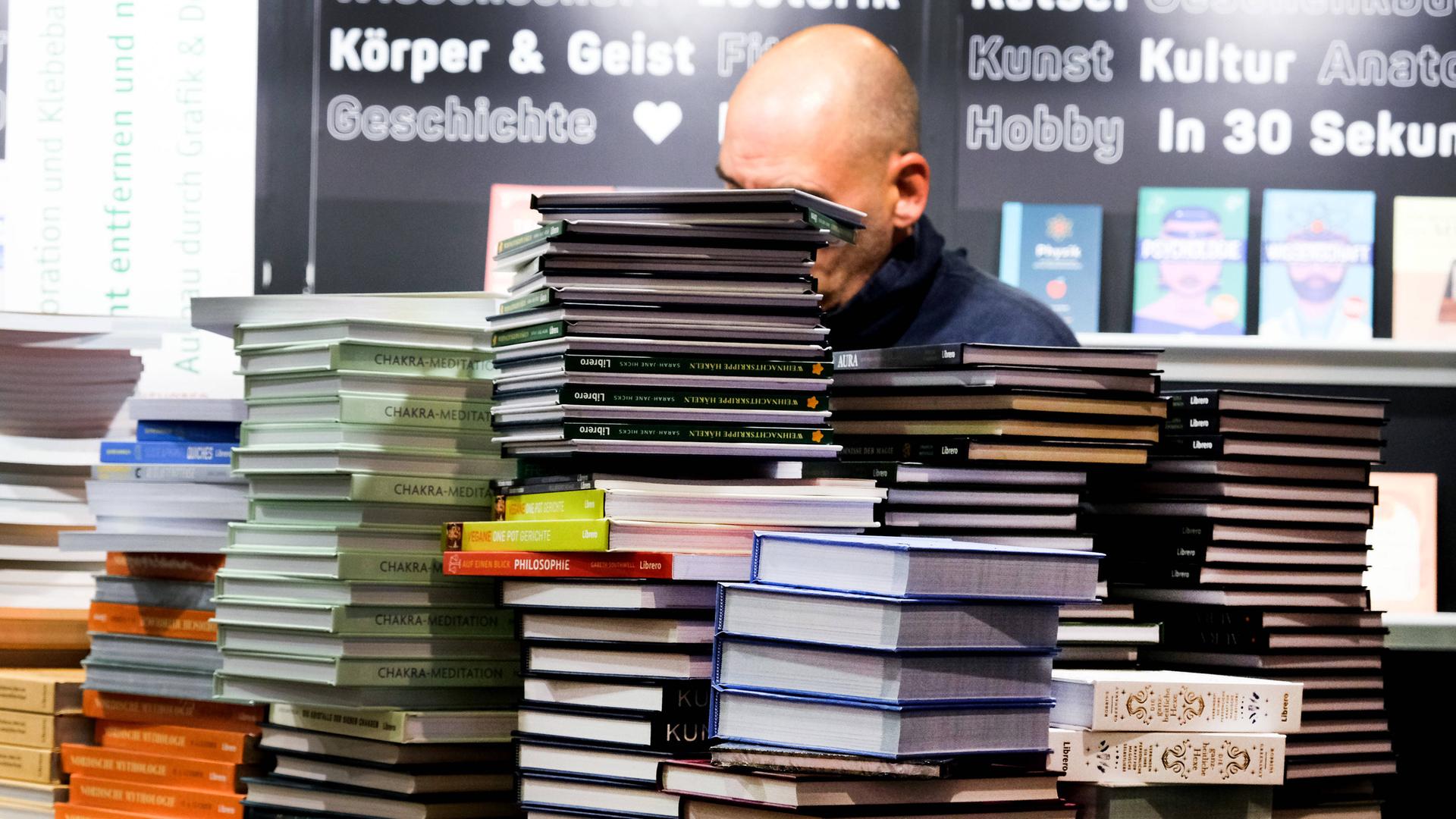 Viele Bücher stapeln sich auf einem Tisch. Der Tisch steht auf der Buch-Messe.