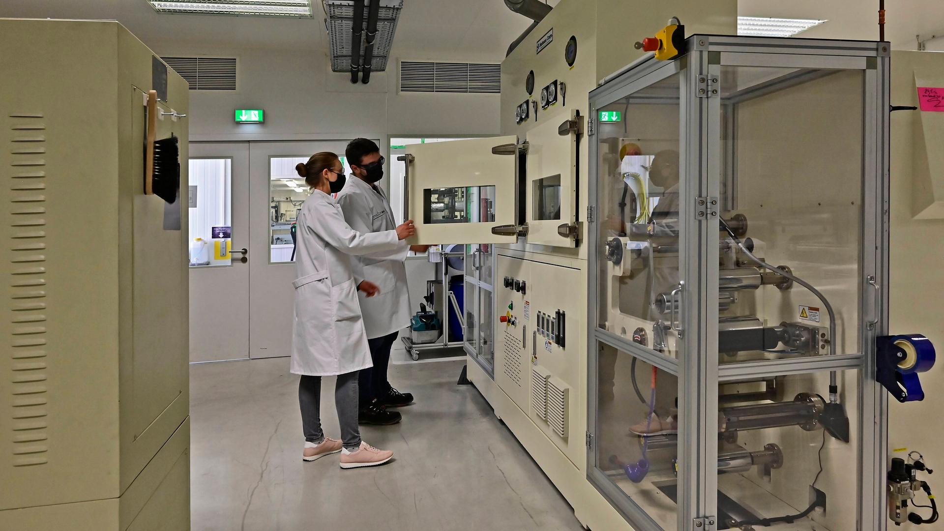 Zwei Personen mit weißen Kitteln in einer laborartigen Umgebung.