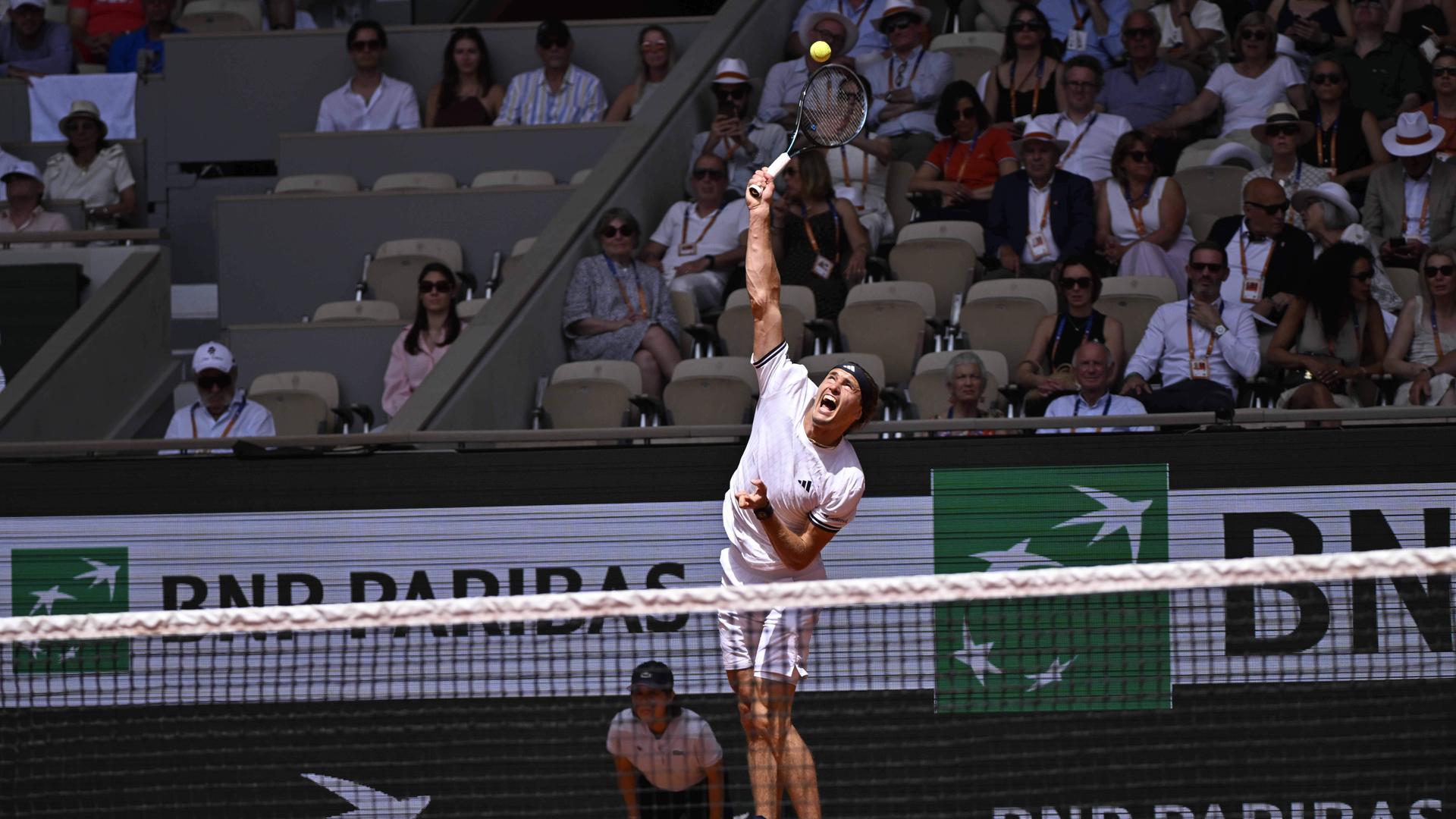 Alexander Zverev springt, um mit seinem Tennisschläger den Ball zu erreichen. Im Hintergrund sitzen mehrere Menschen auf der Besuchertribüne. 