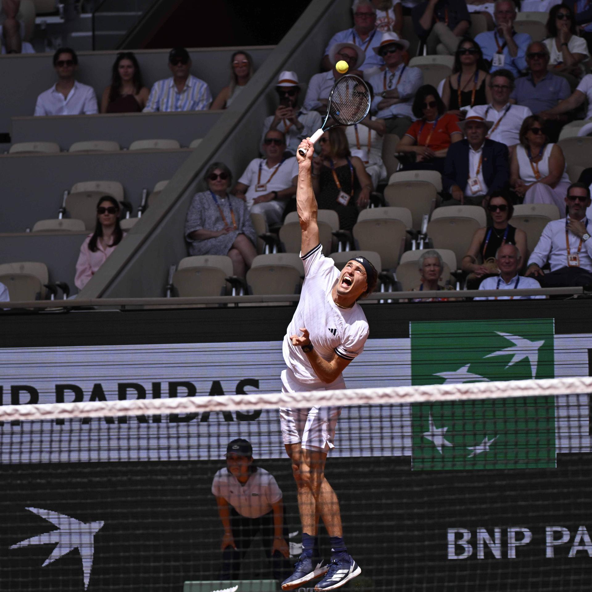 Alexander Zverev springt, um mit seinem Tennisschläger den Ball zu erreichen. Im Hintergrund sitzen mehrere Menschen auf der Besuchertribüne. 