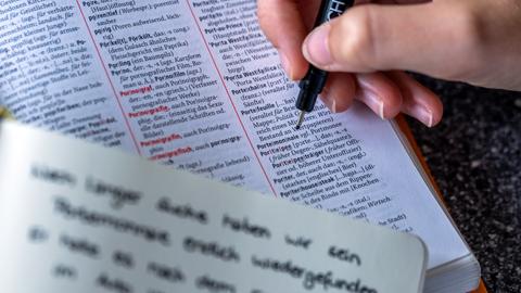 Ein Stift deutet auf die Worte "Portemonnaie" und im Vergleich dazu "Portmonee" auf einer Seite des Duden mit den Regeln der deutschen Rechtschreibung.