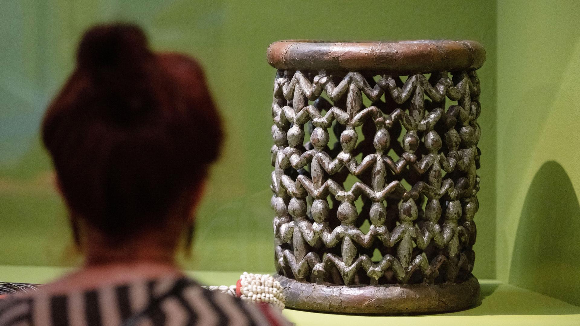 Hinter einer Vitrine in einem Museum befindet sich ein Thronhocker aus Kamerun.