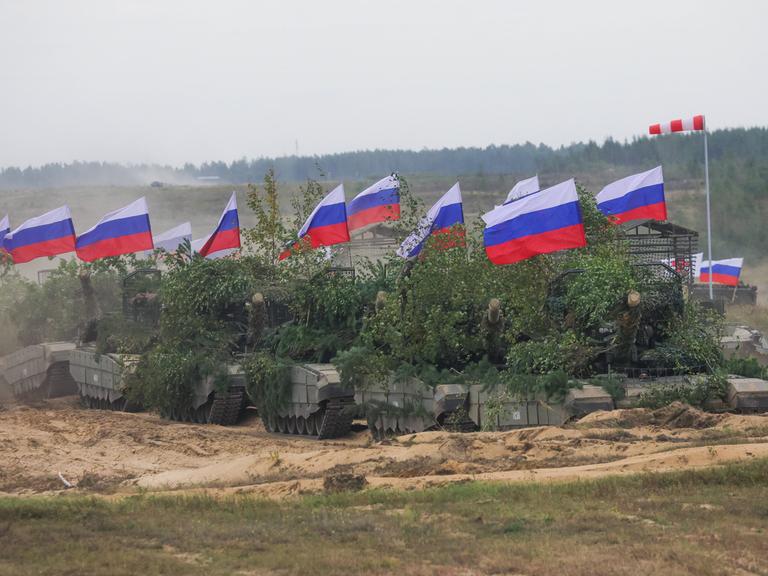 Mit grünen Pflanzen getarnte russische Panzer mit Fahnen bei der Militärübung Zapad 2025