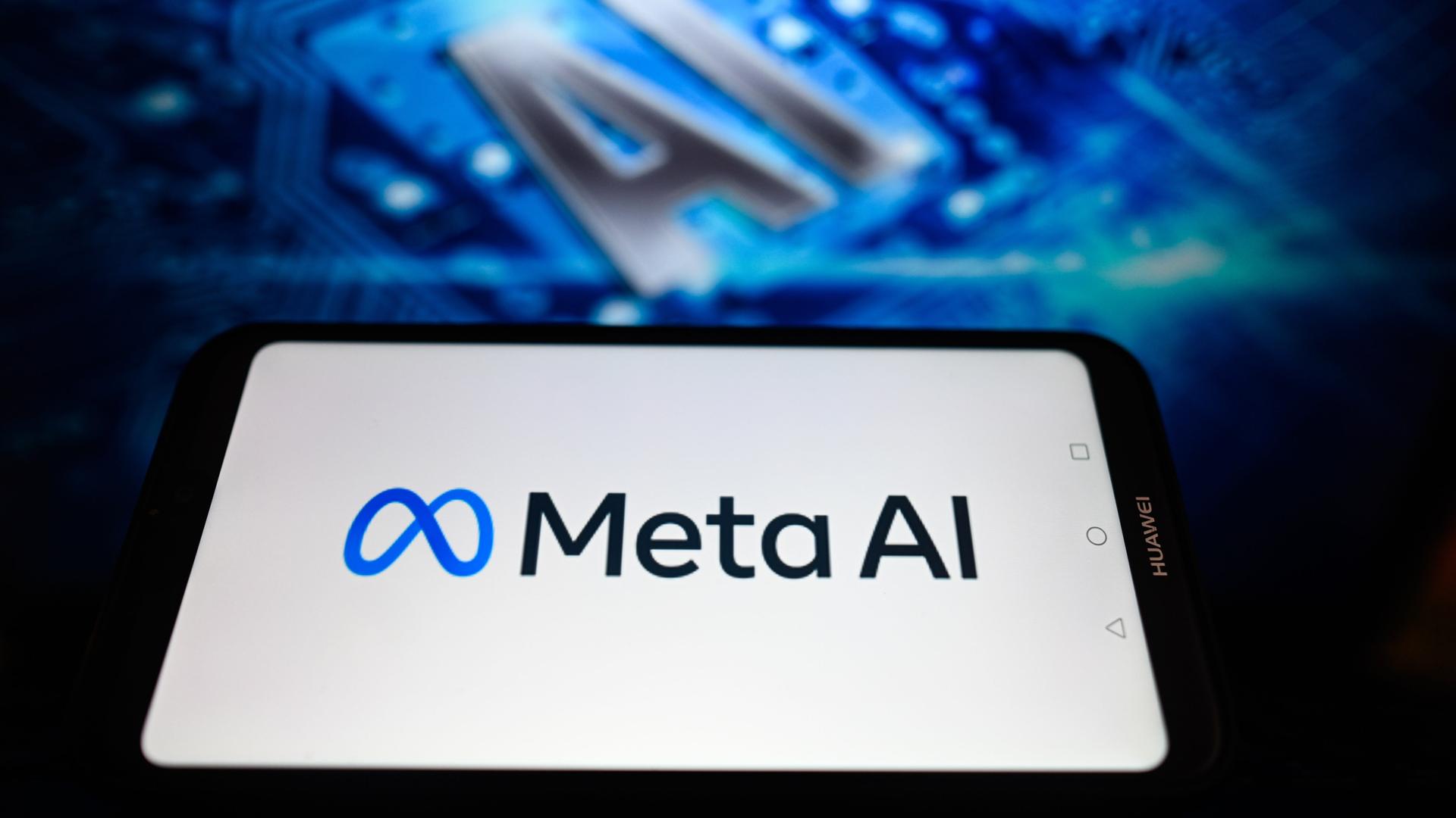 Auf der Illustration wird das Logo des Facebook-Konzerns Meta und der Schriftzug Meta AI auf einem Smartphone angezeigt. Im Hintergrund etwas unscharf die Buchstaben "AI"