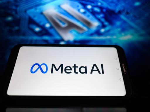 Auf der Illustration wird das Logo des Facebook-Konzerns Meta und der Schriftzug Meta AI auf einem Smartphone angezeigt. Im Hintergrund etwas unscharf die Buchstaben "AI"