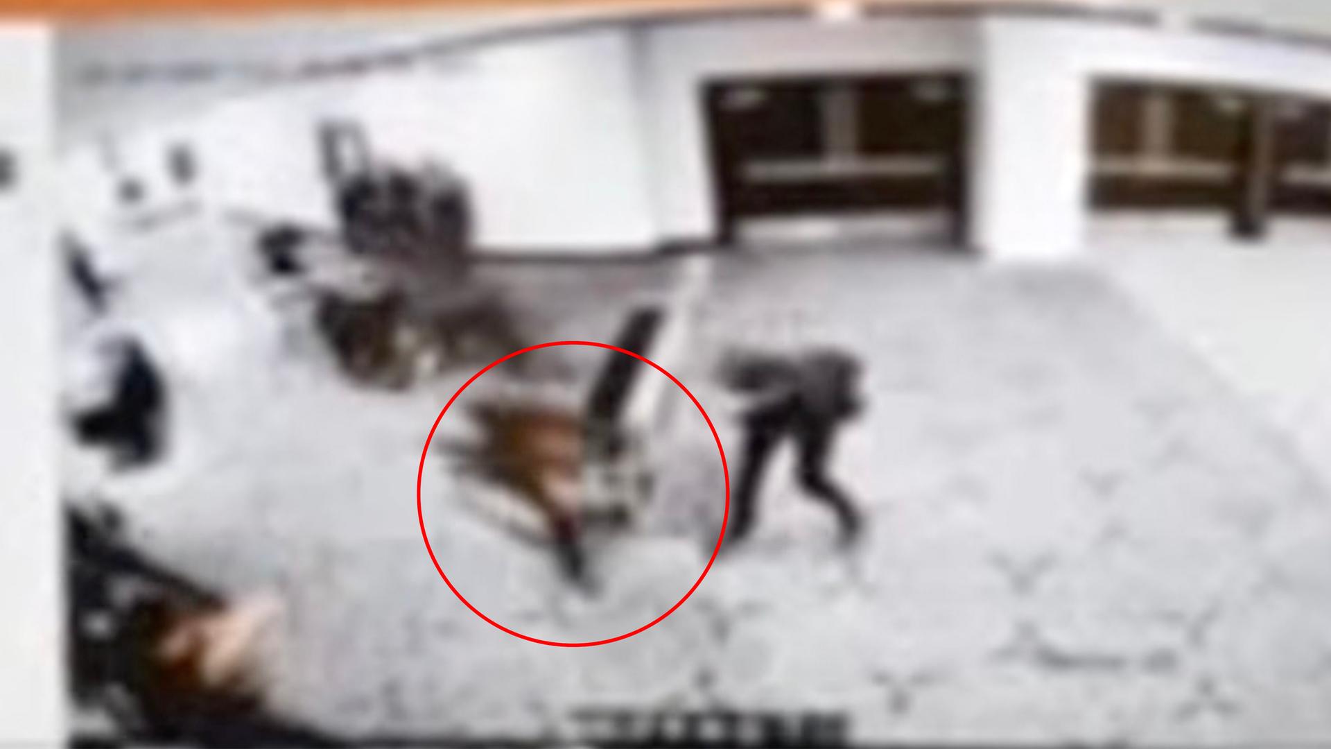 Das Bild ist sehr unscharf: Man sieht den Täter in einem Flur zur Erkennung rot eingekreist, außerdem mehrere Sicherheitsleute.