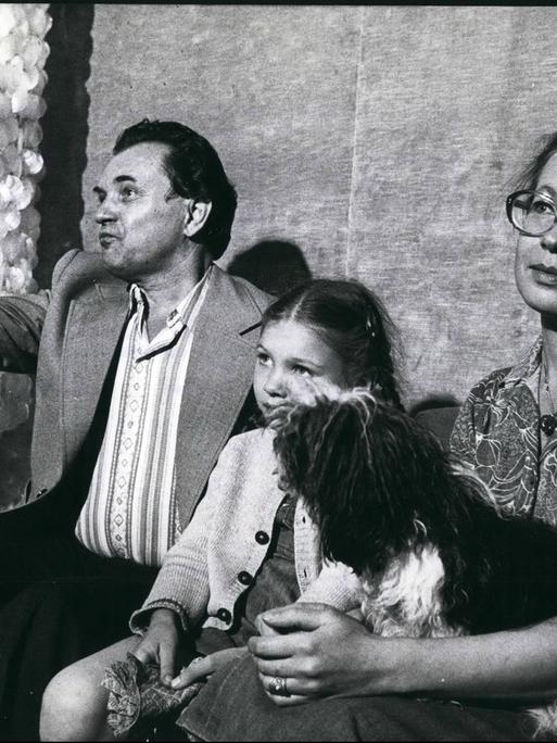 Auf dem Schwarz-weiß-Bild sind ein Mann, ein Kind und eine Frau zu sehen, die auf einer Bank sitzen. Auf dem Schwarz-weiß-Bild sind ein Mann, ein Kind und eine Frau zu sehen, die auf einer Bank sitzen.