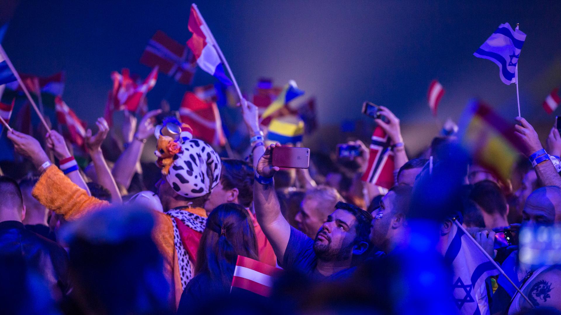 Fans stehen während der ESC-Show im Publikum, schwenken die Flaggen verschiedener Länder und machen Selfies.