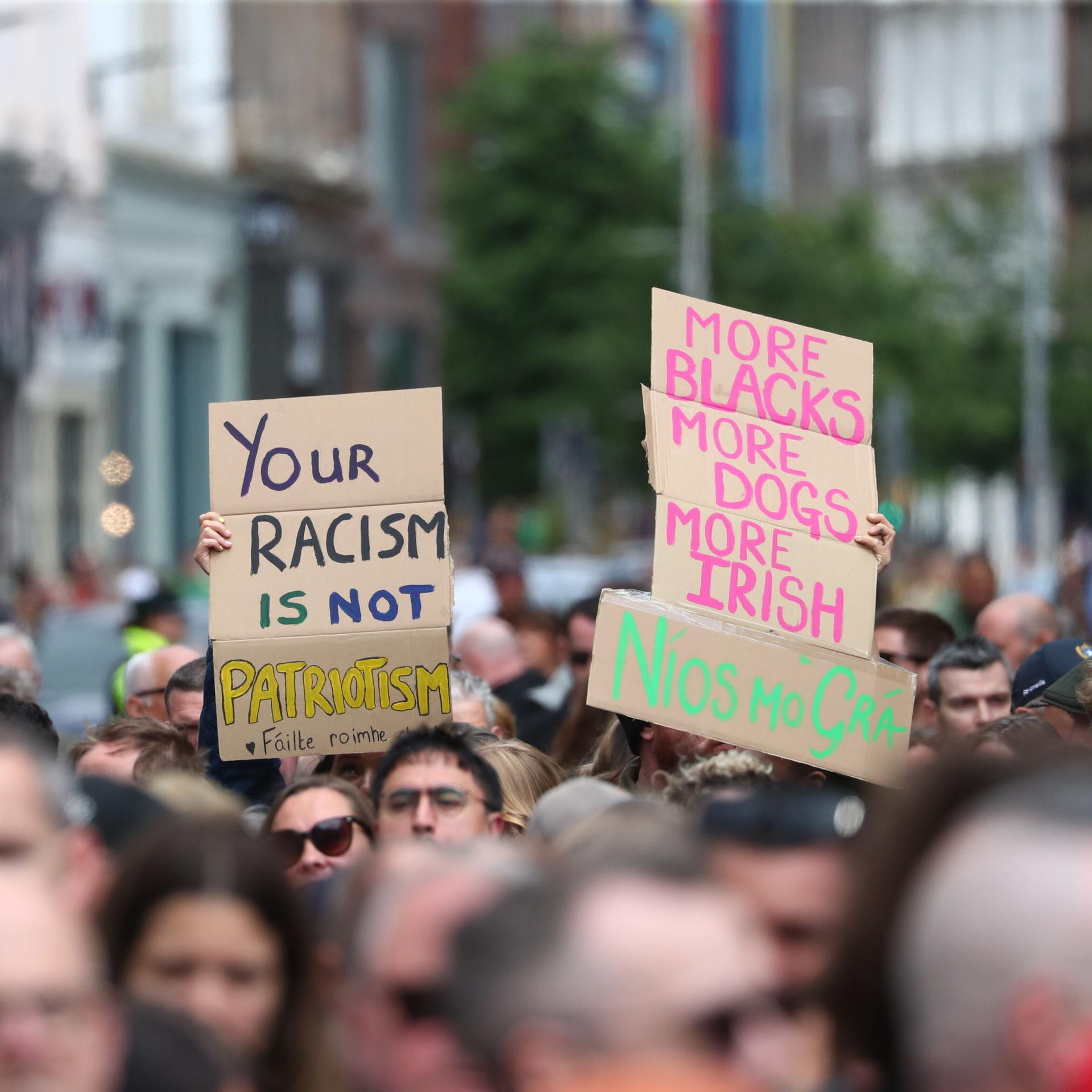 Demonstranten halten Plakate mit Aufschriften wie "Euer Rassismus ist kein Patriotismus" in die Höhe 