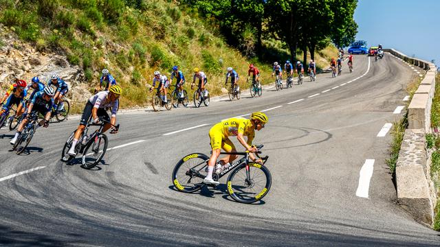Radprofis bei der Tour de France fahren hintereinander eine Bergstraße entlang. 