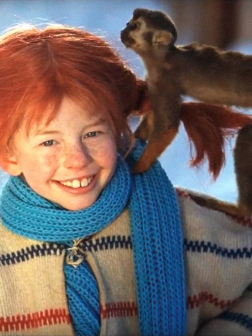 Ein rothaariges Mädchen mit abstehenden Zöpfen trägt einen Wollpullover und hat einen Schal um den Kopf gewickelt. Auf ihrer Schulter ist ein kleines Äffchen.