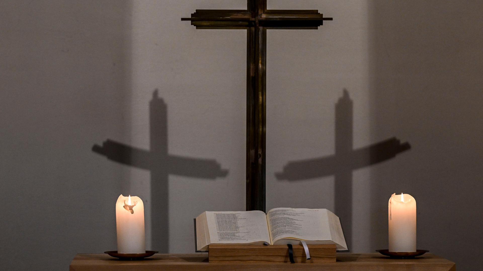 Brennende Kerzen und ein Kreuz in einer Kapelle.