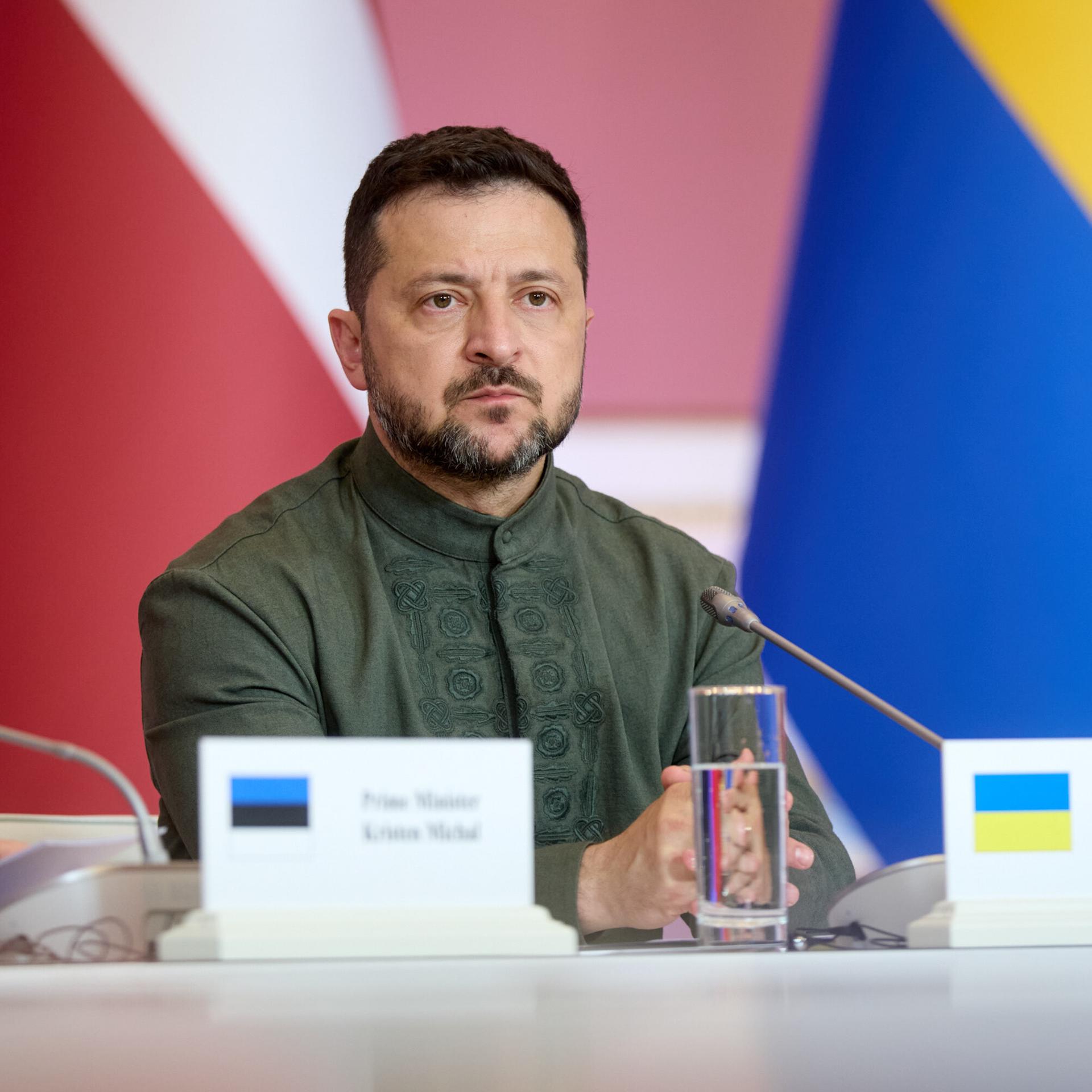 Wolodymyr Selenskyj sitzt in Kiew an einem Tisch und schaut ernst. 