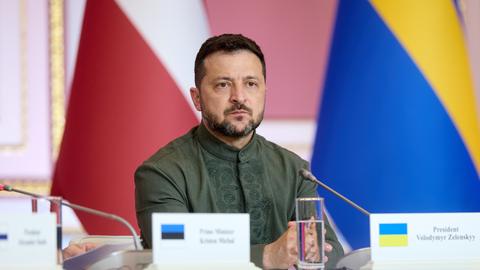 Wolodymyr Selenskyj sitzt in Kiew an einem Tisch und schaut ernst. 