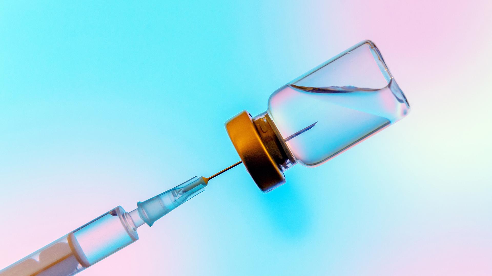Studioaufnahme einer Spritze, die Flüssigkeit, einen Impfstoff, aus einem Gefäß zieht.