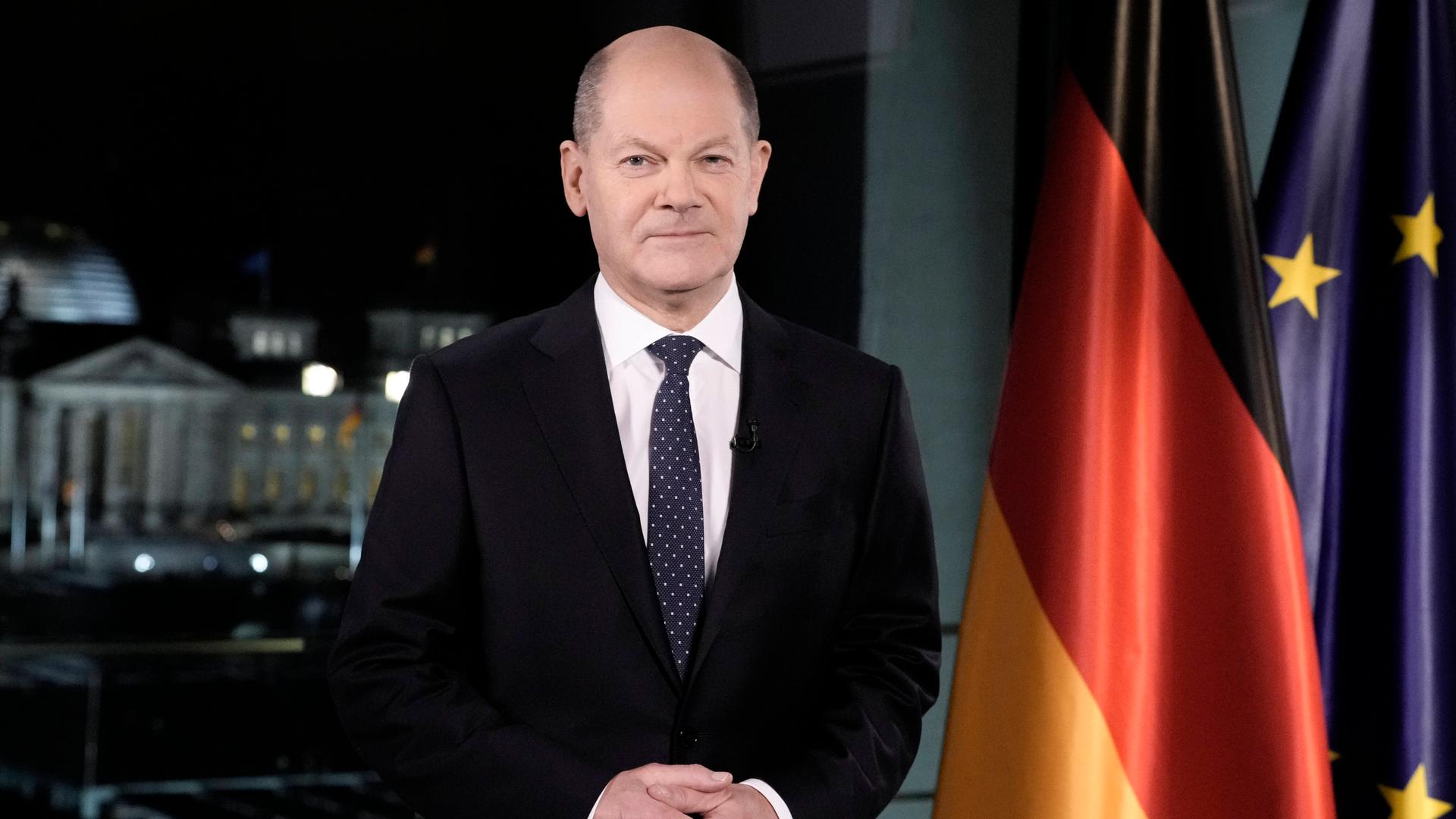 Bundeskanzler Olaf Scholz steht während seiner Neujahrsansprache vor den Flaggen Deutschlands und der EU.