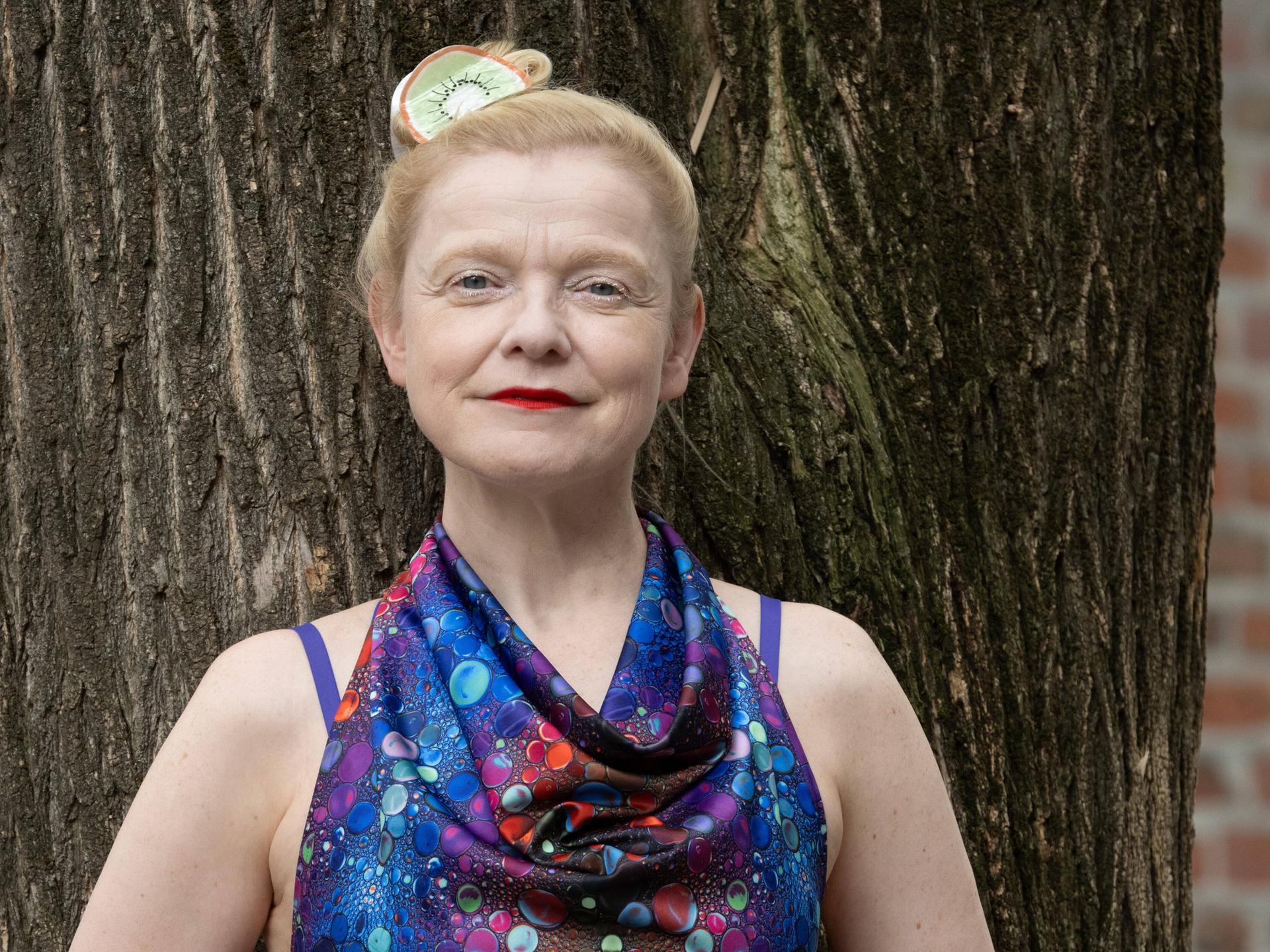 Sasa Hanten lehnt in einem bunten Kleid an einem Baum.
