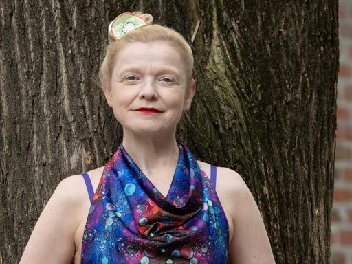 Sasa Hanten lehnt in einem bunten Kleid an einem Baum. Sasa Hanten lehnt in einem bunten Kleid an einem Baum.