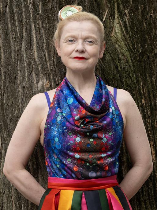 Sasa Hanten lehnt in einem bunten Kleid an einem Baum. Sasa Hanten lehnt in einem bunten Kleid an einem Baum.