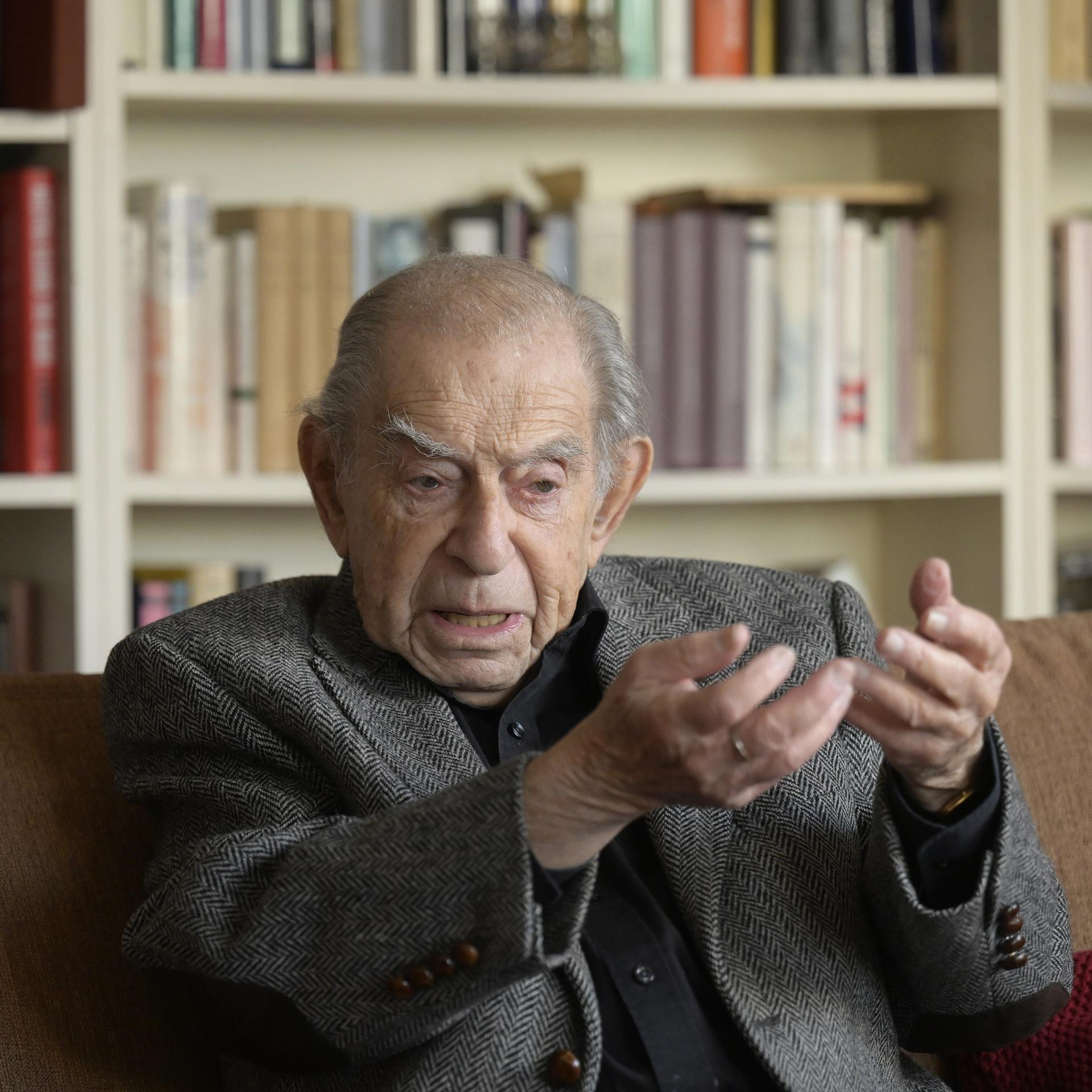 Der hochbetagte Publizist und TV-Moderator Paul Lendvai während eines Interviews. Er sitzt auf einem Sofa vor einem Bücherregal und gestikuliert.