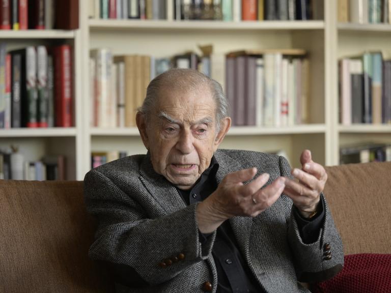 Der hochbetagte Publizist und TV-Moderator Paul Lendvai während eines Interviews. Er sitzt auf einem Sofa vor einem Bücherregal und gestikuliert.