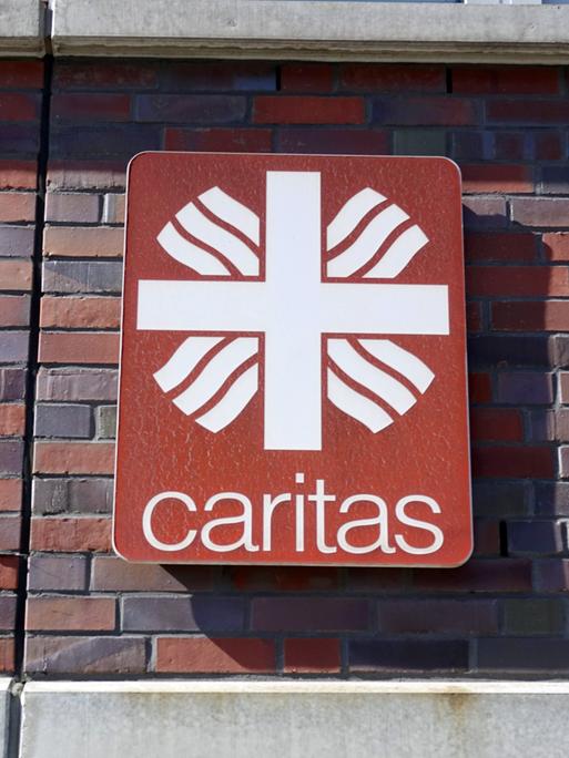 Das Logo der Caritas, des Deutschen Caritasverbandes, hängt an einer Hauswand. Die Caritas ist ein Wohlfahrtsverband der römisch-katholischen Kirche in Deutschland. Er ist als eingetragener Verein organisiert.