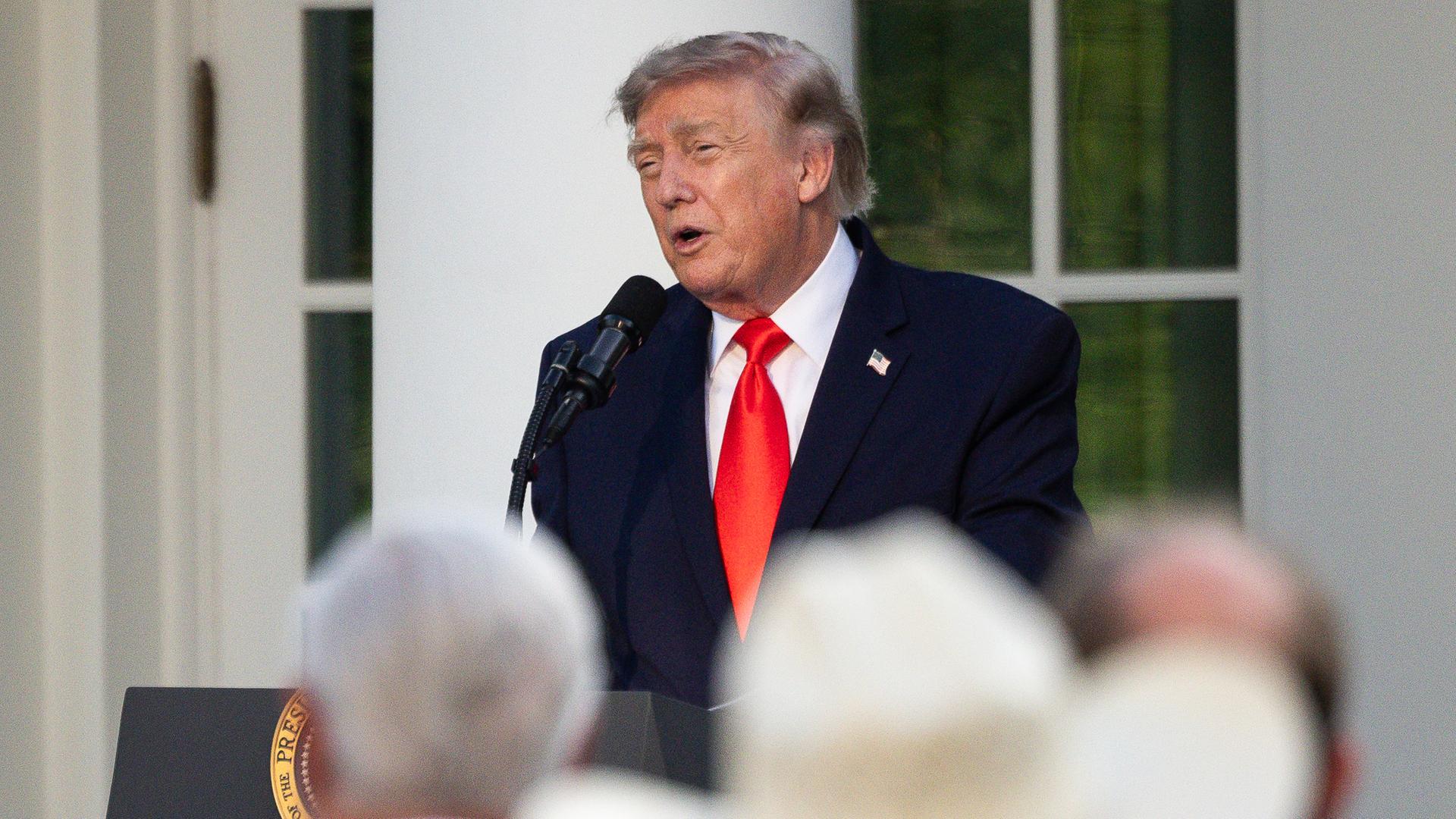 Donald Trump spricht an einem Rednerpult zu einer Gruppe von Menschen. Im Vordergrund steht eine Person mit einem großen Cowboyhut.