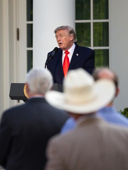 Donald Trump spricht an einem Rednerpult zu einer Gruppe von Menschen. Im Vordergrund steht eine Person mit einem großen Cowboyhut.