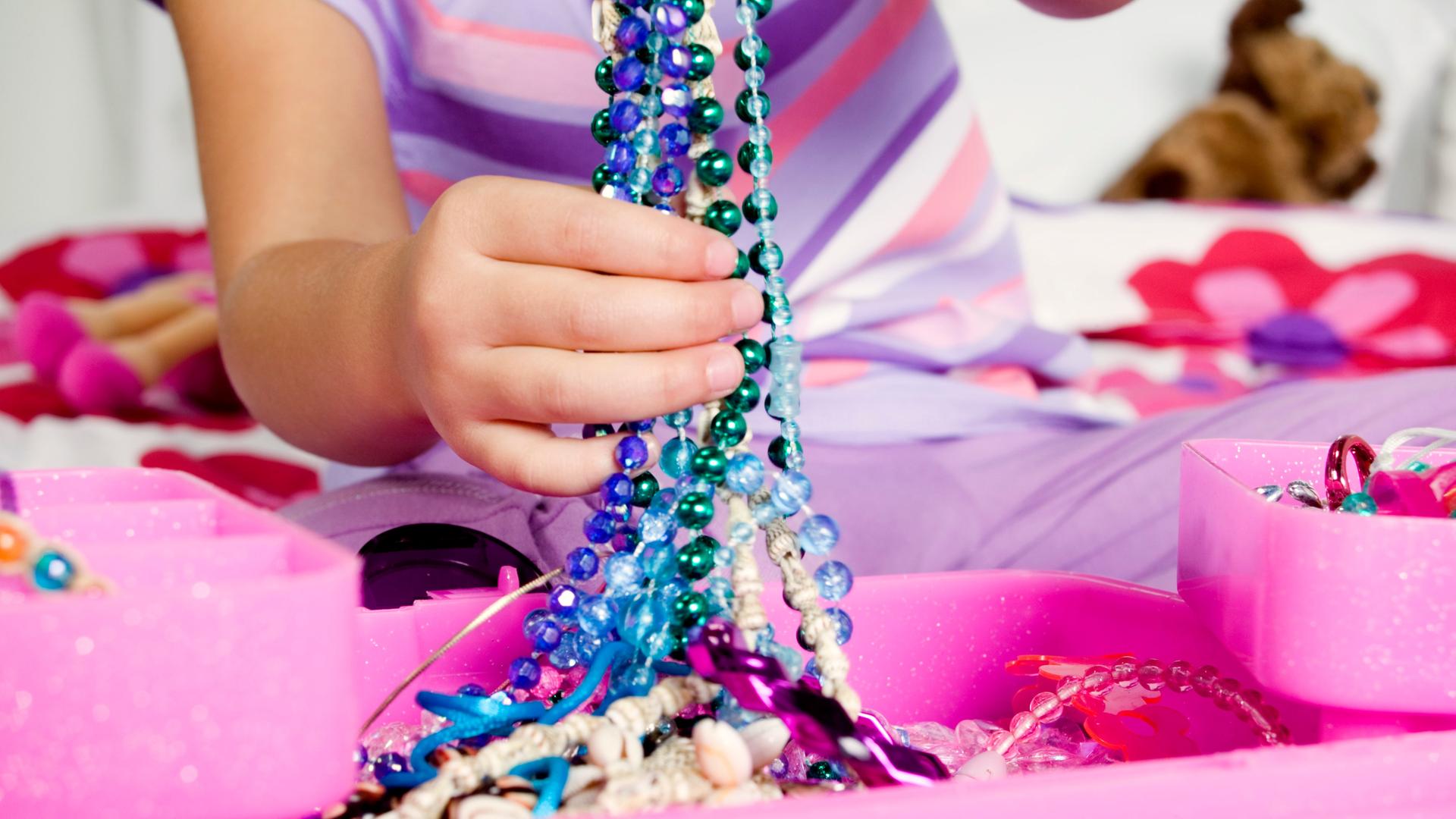 Eine Kinderhand hält bunte Glasperlenketten hoch
