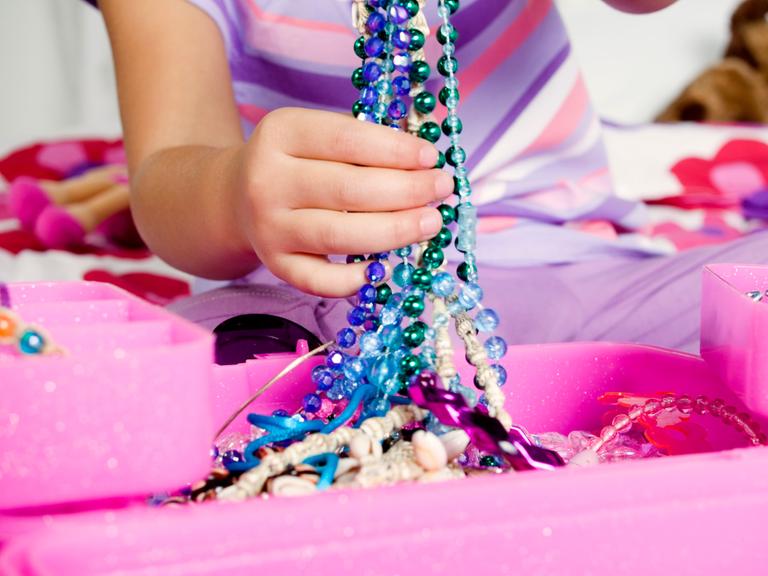 Eine Kinderhand hält bunte Glasperlenketten hoch
