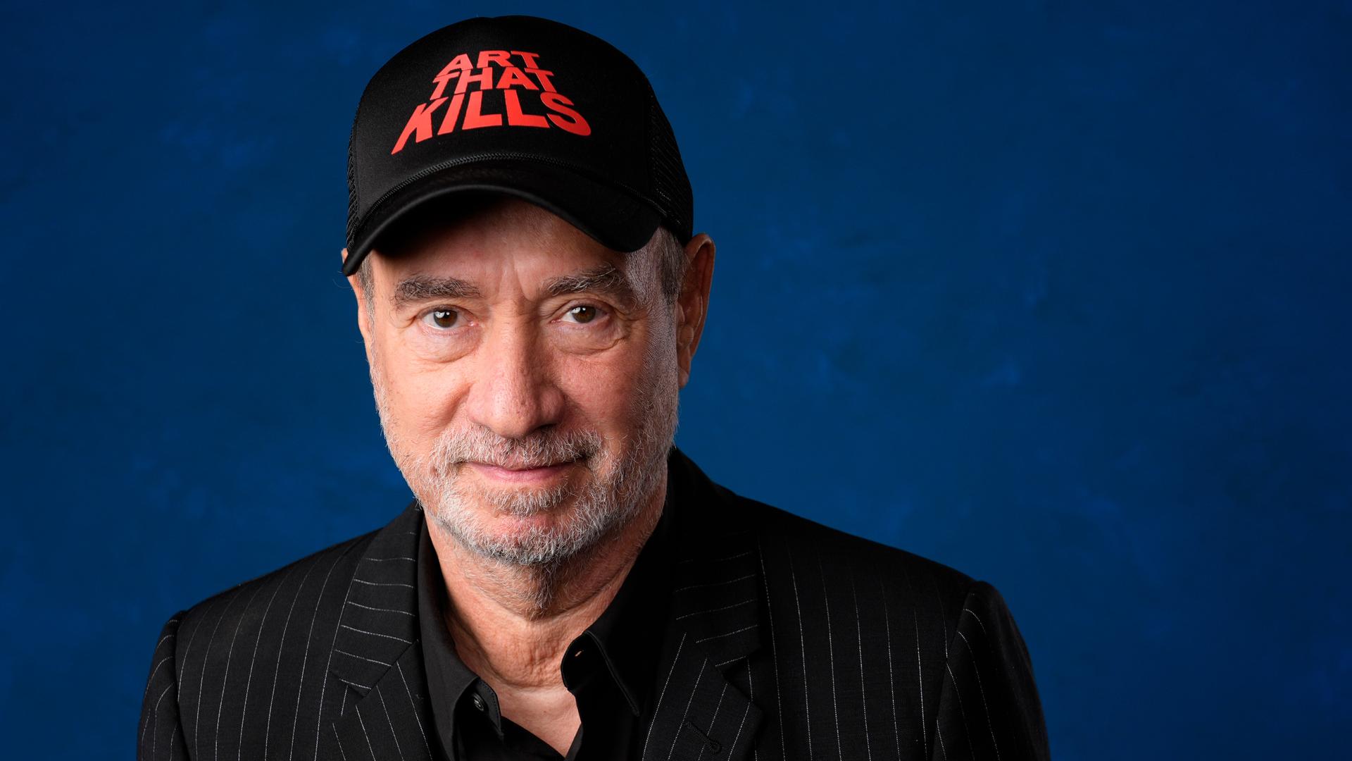 Roland Emmerich in einer Porträt-Aufnahme mit einer schwarzen Kappe, die die Aufschrift trägt "Art that kills"