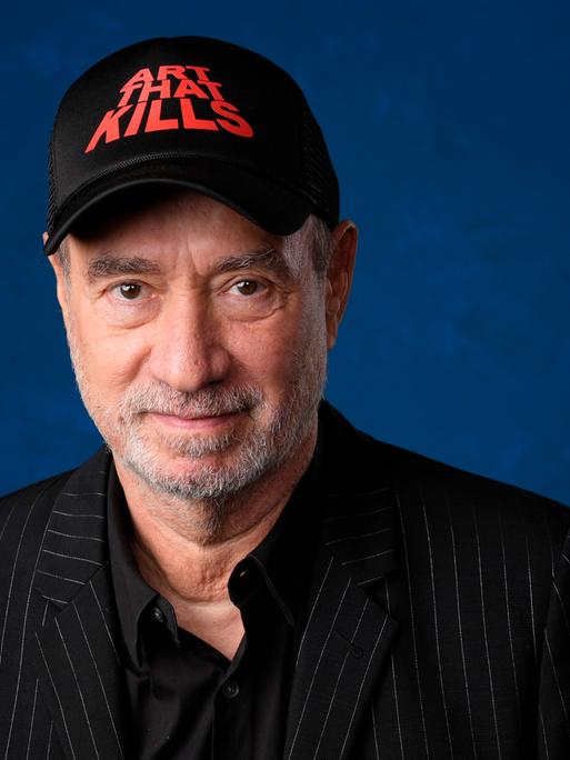 Roland Emmerich in einer Porträt-Aufnahme mit einer schwarzen Kappe, die die Aufschrift trägt "Art that kills"