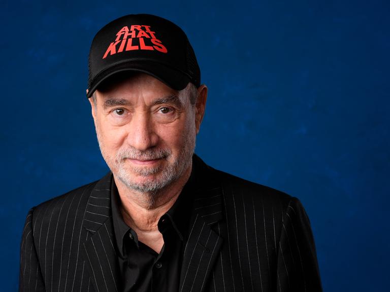 Roland Emmerich in einer Porträt-Aufnahme mit einer schwarzen Kappe, die die Aufschrift trägt "Art that kills"