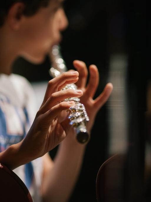 Ein Kind leicht unscharf in der Bildmitte, eine silberne im Vordergrund befindliche Querflöte spielend.