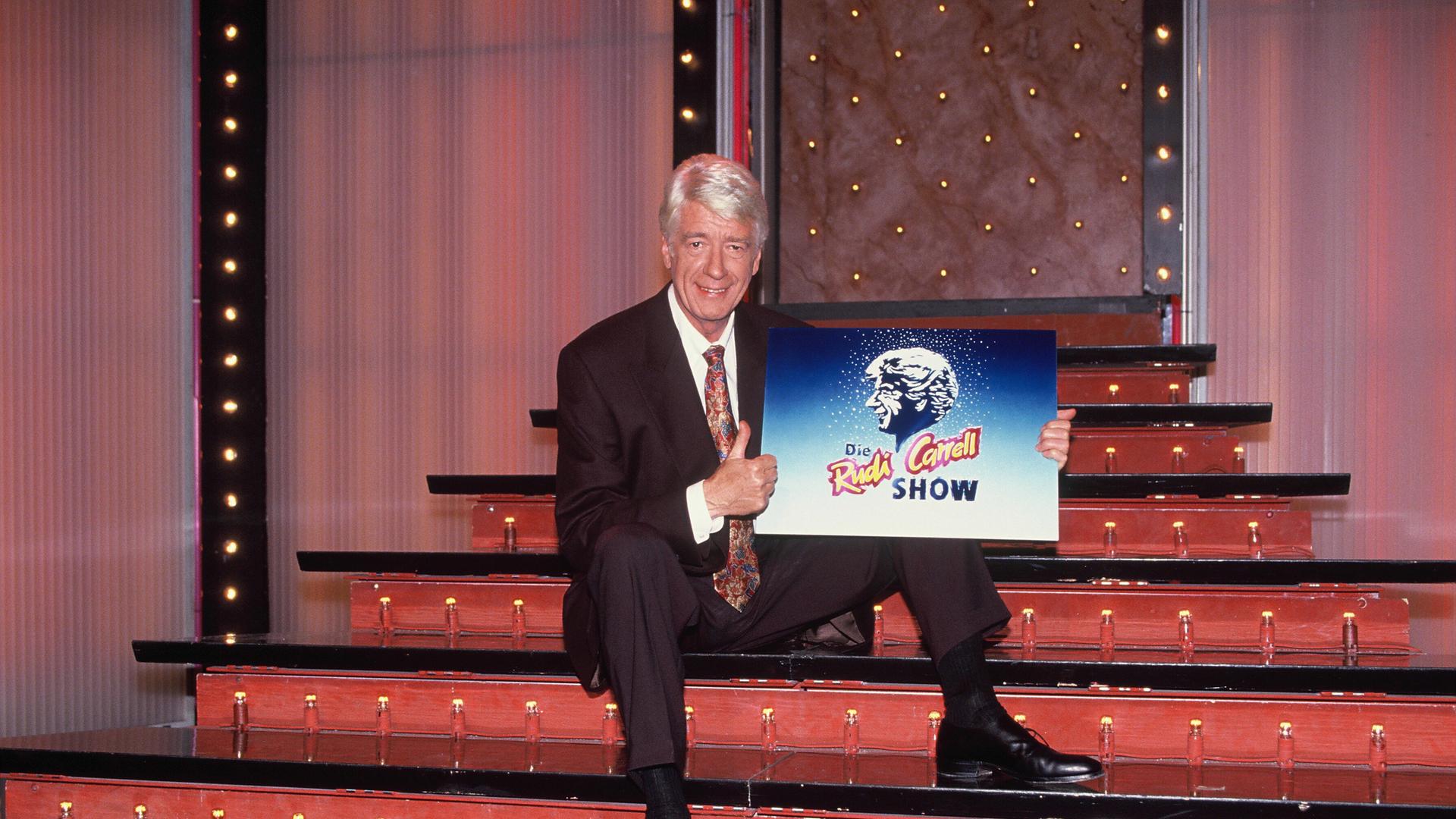 Showmaster und Entertainer Rudi Carrell posiert mit dem Logo der Rudi Carrell Show auf der Showtreppe im Jahre 1992