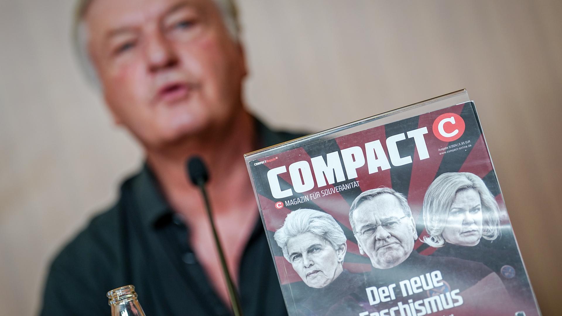 Jürgen Elsässer gibt eine Pressekonferenz zur Aufhebung des Verbots der Zeitschrift "Compact" durch das Bundesverwaltungsgerichts hinter einem Titelbild seines Magazins. 