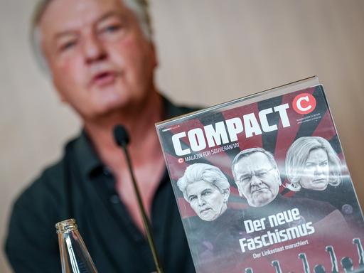 Jürgen Elsässer gibt eine Pressekonferenz zur Aufhebung des Verbots der Zeitschrift "Compact" durch das Bundesverwaltungsgerichts hinter einem Titelbild seines Magazins. 