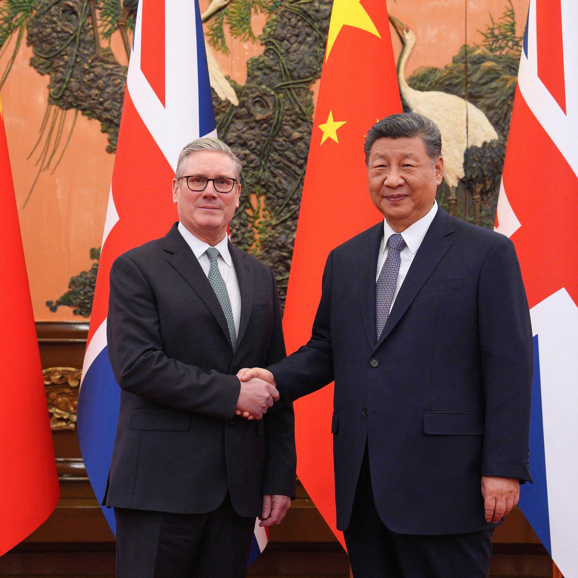 Chinas Präsident Xi Jinping (R) and der britische Premierminister Keir Starmer schütteln sich die Hände. Im Hintergrund sind die Flaggen ihrer beiden Länder zu sehen. 