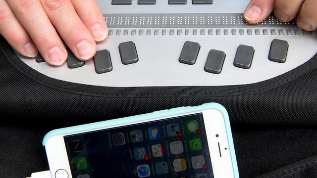 Ein Mann bedient mit einer Braillezeile und Kopfhörern sein Smartphone.