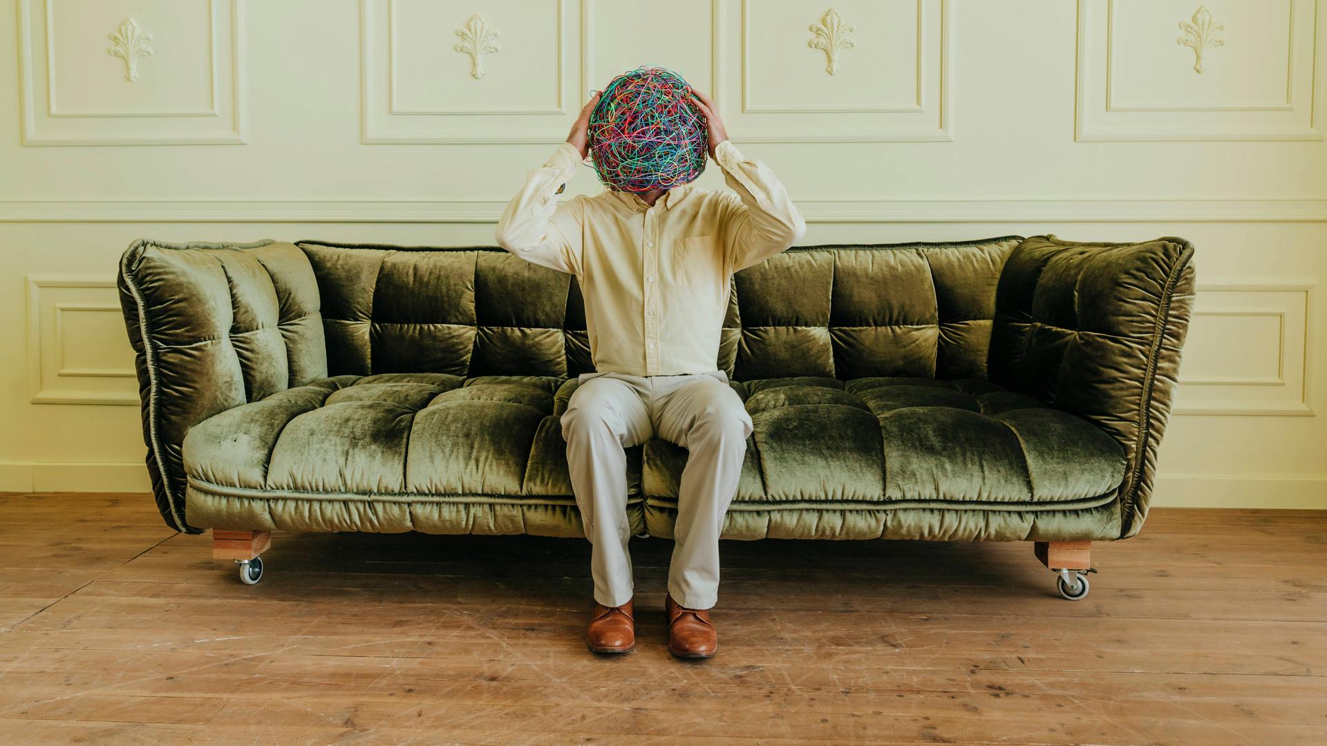 Ein Mann hält seinen Kopf, der aus einem Knäuel von Fäden besteht, der Neurodivergenz symbolisieren soll